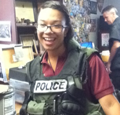 A young woman similing at the camera wearing a bulletproof vest