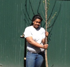 A young woman looking at the camera holding a small tree