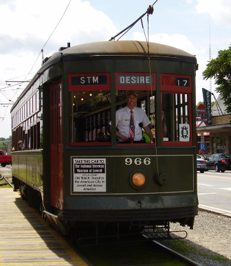 A man driving a green trolley smiling as he poses for a picture with the trolley