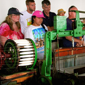 A group of men, women, and children looking at a machine that makes cloth