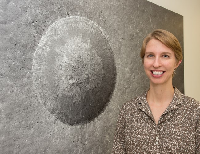 A woman stands in front of a photo of the moon's surface.