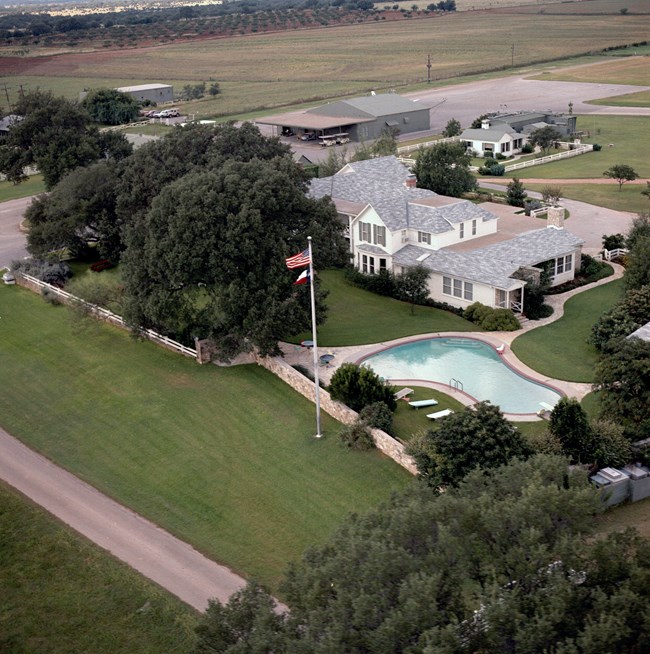 Aerial view of a large, two-story white frame house and swimming pool.