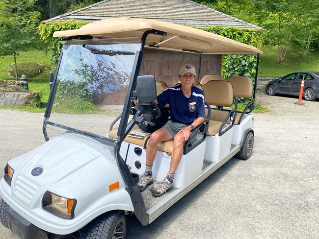 park volunteer in blue polo sits in drivers seat of extended electric golf cart