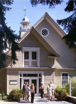 Visitors linger in the sun in front of the beige three-story renovated barn, whose steepled dormers point toward the blue sky. NPS Photo.