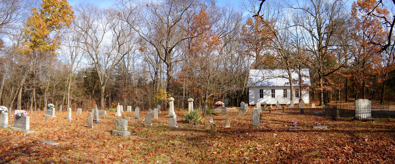 A open cemetery with headstones and a small church in the background.