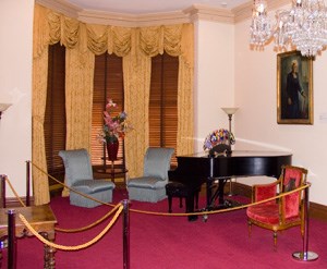 A piano and sitting chairs beneath a portrait of Ms. Bethune.