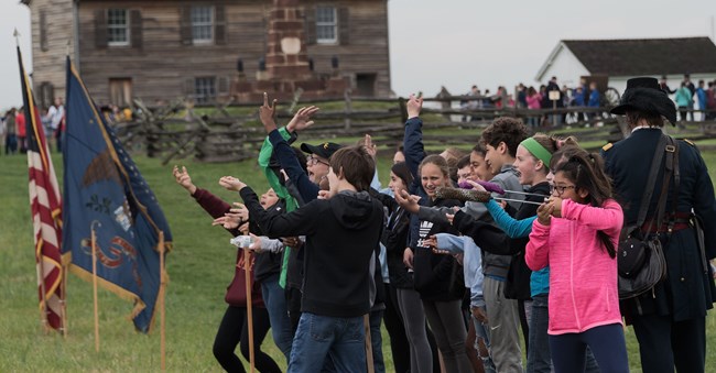 A group of students is charging toward flags while a man in a soldier uniform paces behind them.