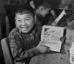 A smiling boy holds up his reading book
