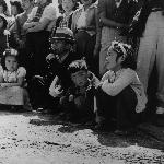 Family sits on a curb with a crowd behind
