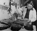 Man using an iron to press a stack of work caps