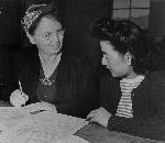 Two women fill out paper forms