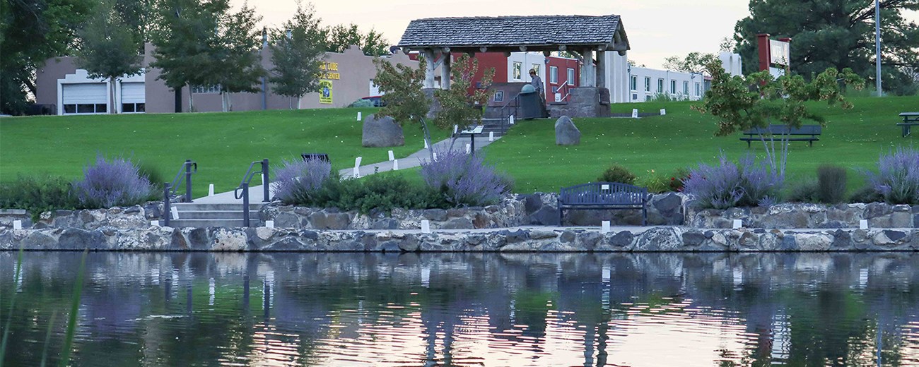 Luminarias line a sidewalk by a pond and lead up stairs to a small structure.