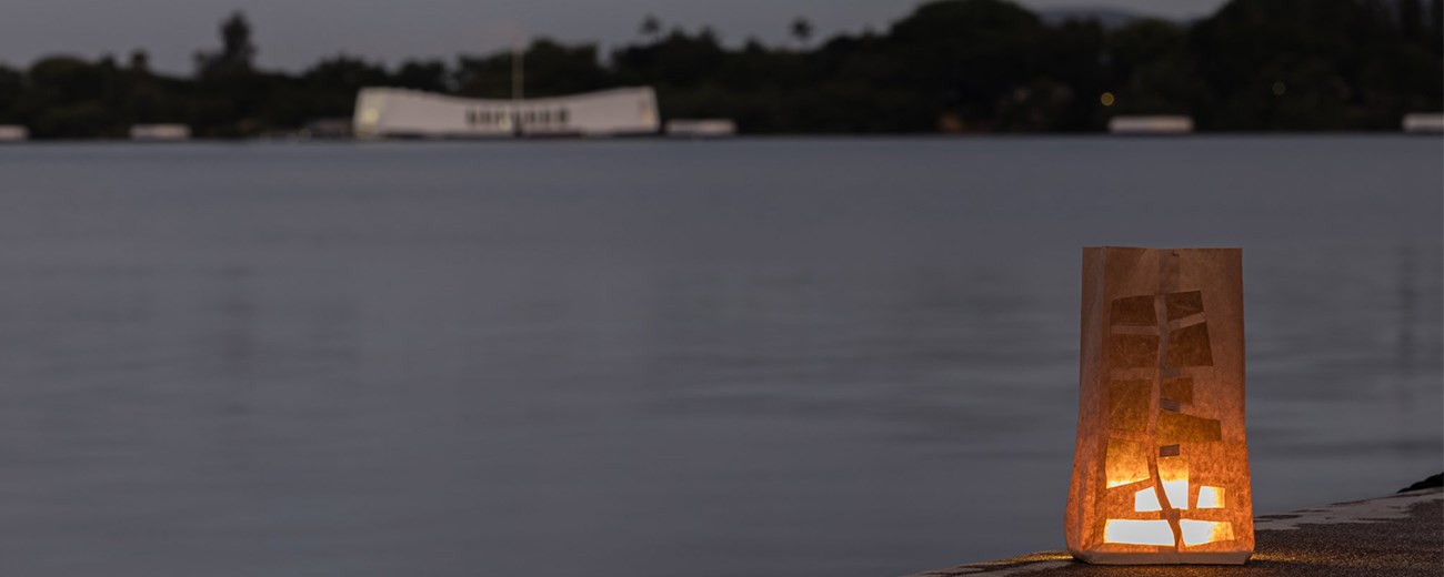 A luminaria is aglow with water and a white structure in the background.