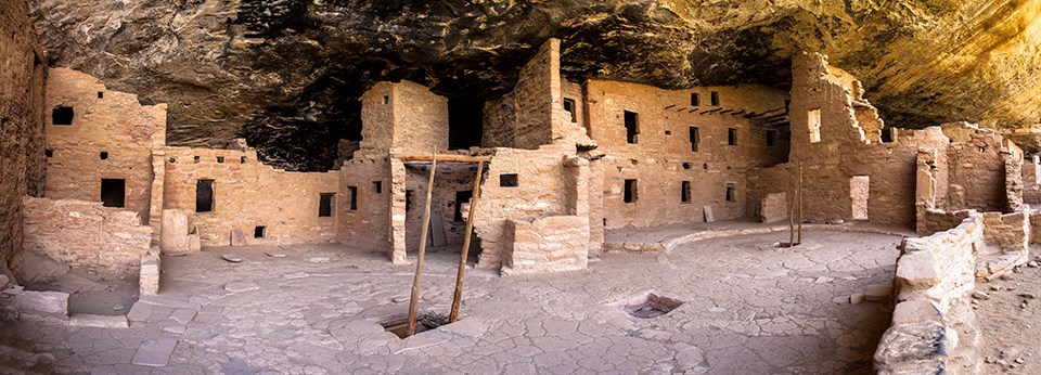 Kiva courtyard showing kiva roof, kiva entrance, and ladder with pueblo rooms in background