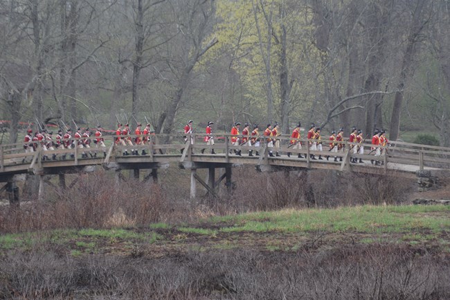 A group of British soldiers march over a wooden bridge