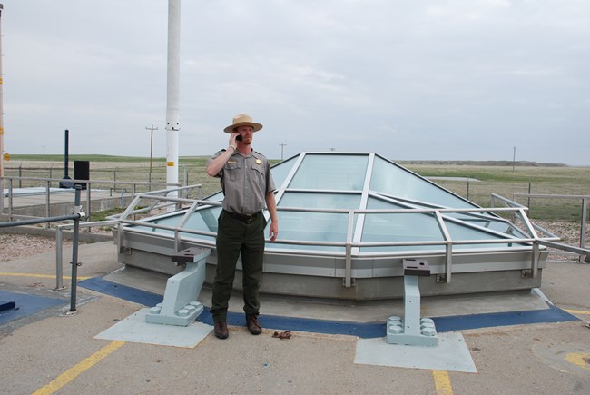 Park ranger listening on a cell phone standing beside a missile silo