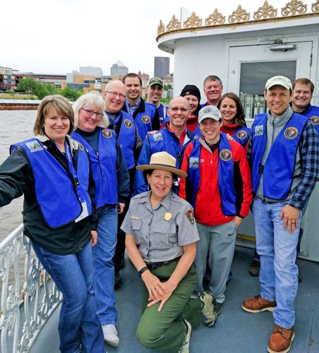 Happy volunteers in blue vest surrounding a park ranger on a boat.