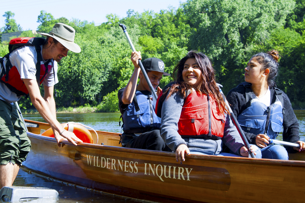 A park ranger holds a wooden boat with three people inside