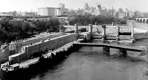 A lock and dam under construction. A cityscape with grain silos sits in the background.