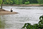 A person sits on a sandy bank at the confluence of two rivers.