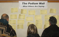 People gather at the bulletin board to review comments on notes left by Open House participants.