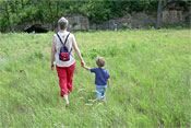 A boy and a woman walks through a grassy area. A rocky bluff rises in the background.