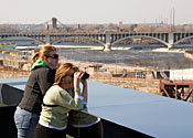 Two people look out over the St. Anthony Falls area, a busy industrial and business district.