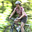 A woman rides a bicycle along a wooded trail.