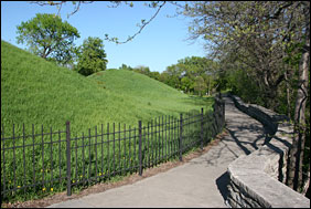 Grass-covered mounds on left are Native American gravesites. A path leads to the right between the mounds and the river bluffs.