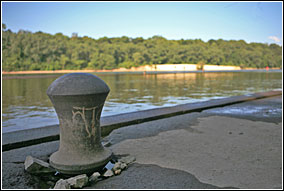 Parts of the Meeker Dam lock system can still be seen during low water. The photo includes the concrete wall and a large station that barges would tie up to. The river is in the background bordered by sand banks and forested shores.