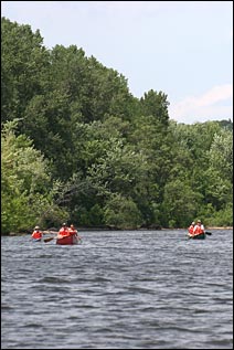 Canoeists paddle down the Mississippi River. Tree-lined bluffs tower in the background.