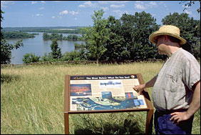 A man reads an interpretive sign that overlooks an island-dotted Mississippi River.