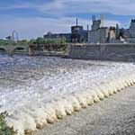 Water cascades over St. Anthony Falls with the Minneapolis skyline in the background.