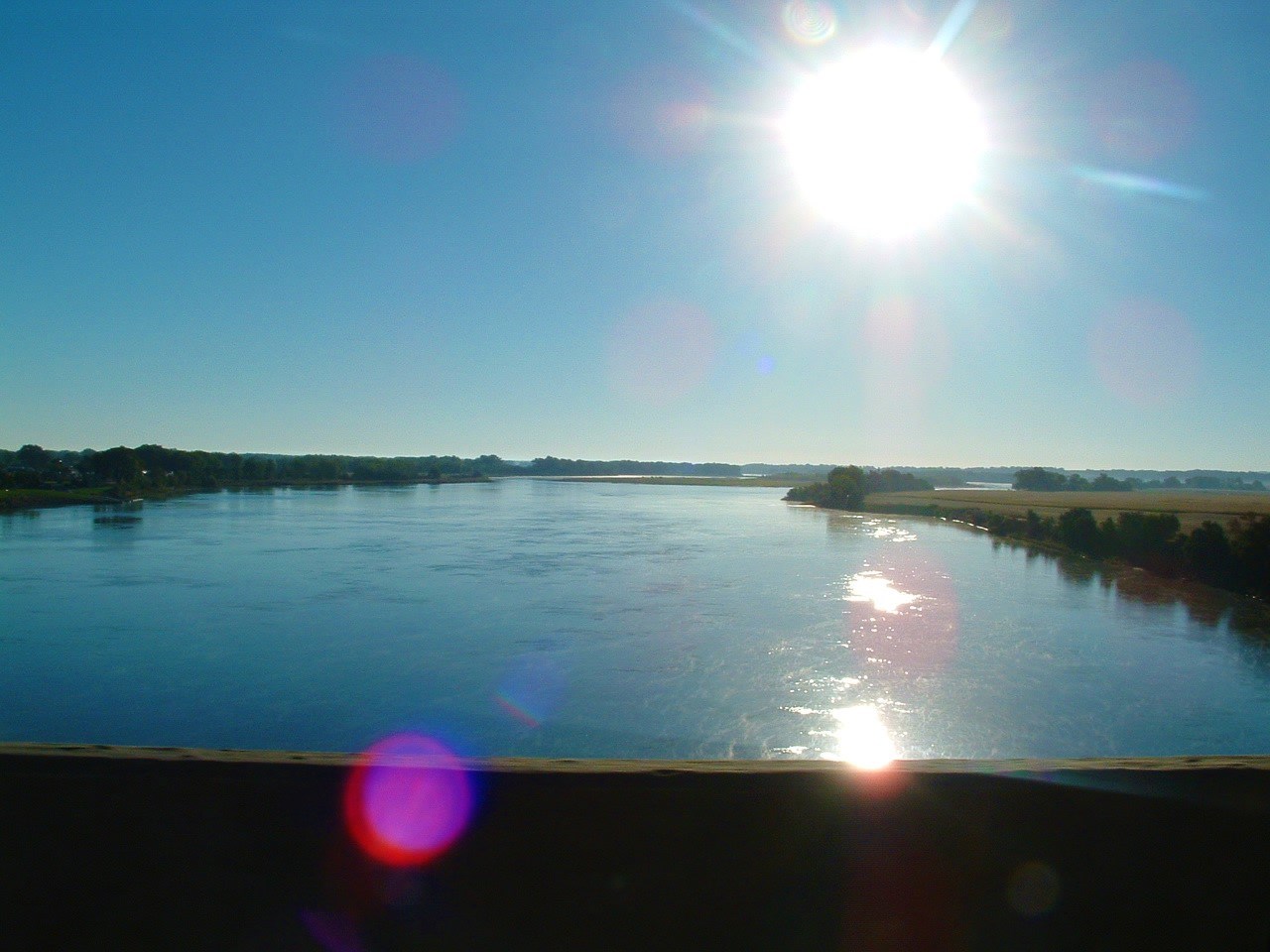Missouri River with river banks on left and right. The sun is in the upper right of the image with a sunflare in the bottom left (purple).