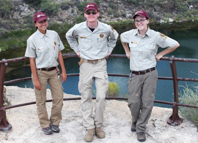 Three youth stand in volunteer uniforms and hats.