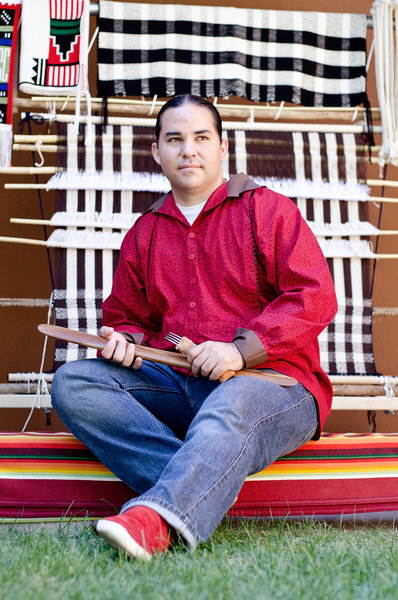 Louie Garcia sits in front of a traditional loom and weavings.