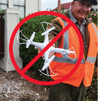 A man in a reflective vest is holding out a drone, and there is a red slash mark through it. No drones are allowed.