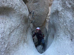 A hiker in the narrow Banshee Canyon at Hole-in-the-Wall climbs the rings trail using the metal circle rings bolted into the canyon wall.