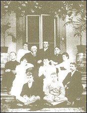 A family with nine children sit on the steps of a house.
