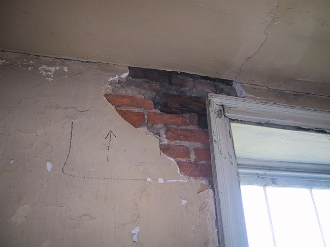Brick is exposed by missing plaster near the upper left corner of a window.