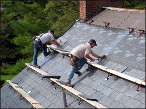Workers install new slate roof on building.