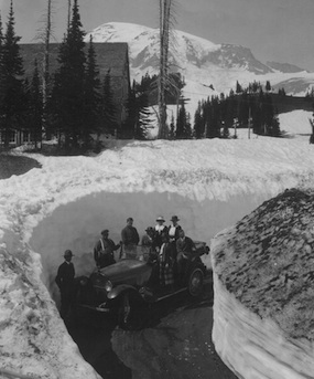Historic photo of early visitors to Mount Rainier, pictured on an old fashioned car between high snow banks.