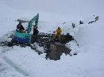 People & machinery work on large puddle in snow
