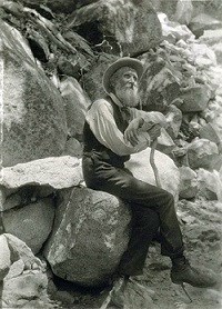 John Muir is sitting on rocks possibly in Yosemite.