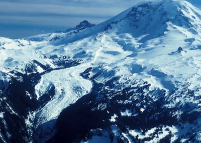 Aerial view of Mount Rainier with the Carbon Glacier curving through a narrow valley down the side of the mountain.