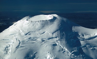 The glacier-capped summit of Mount Rainier, with the roughly circular, rocky rim of the summit crater free of ice and snow.