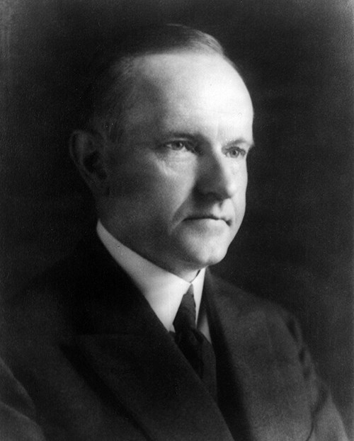 Black and white photograph of Calvin Coolidge looking to the right.  He is a white male with short dark hair combed back and wears a dark suit and tie with a white shirt.