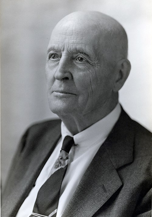 Black and white image of Doane Robinson.  He is a bald, white male in his eighties turned slightly away from the camera and is looking towards the left.  He wears a dark suit, white shirt and necktie.