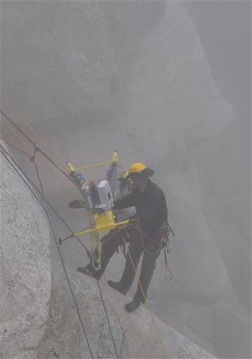Two members of the Mount Rushmore technical ropes team work through the fog to position the custom made tripod on Thomas Jefferson's nose.