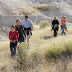 Five people hike through grassland with badlands formations in the background Five people hike through grassland with badlands formations in the background